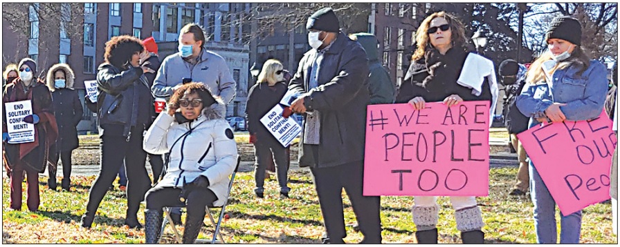 A photo of a crowd of people standing outdoors in Richmond's Monroe Park, holding signs that relate to prison reform. 